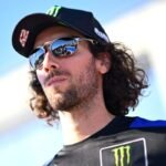 Alex Rins mengenakan topi Yamaha dan kacamata hitam di paddock MotoGP
