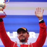 Lewis Hamilton mengenakan seragam Ferrari, mengangkat trofi dan melambaikan tangan di podium Sepang.