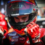 Marc Marquez mengenakan helm dan baju balap Ducati sambil mengepalkan kedua tangan.