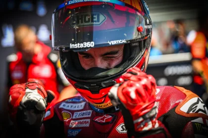Marc Marquez mengenakan helm dan baju balap Ducati sambil mengepalkan kedua tangan.