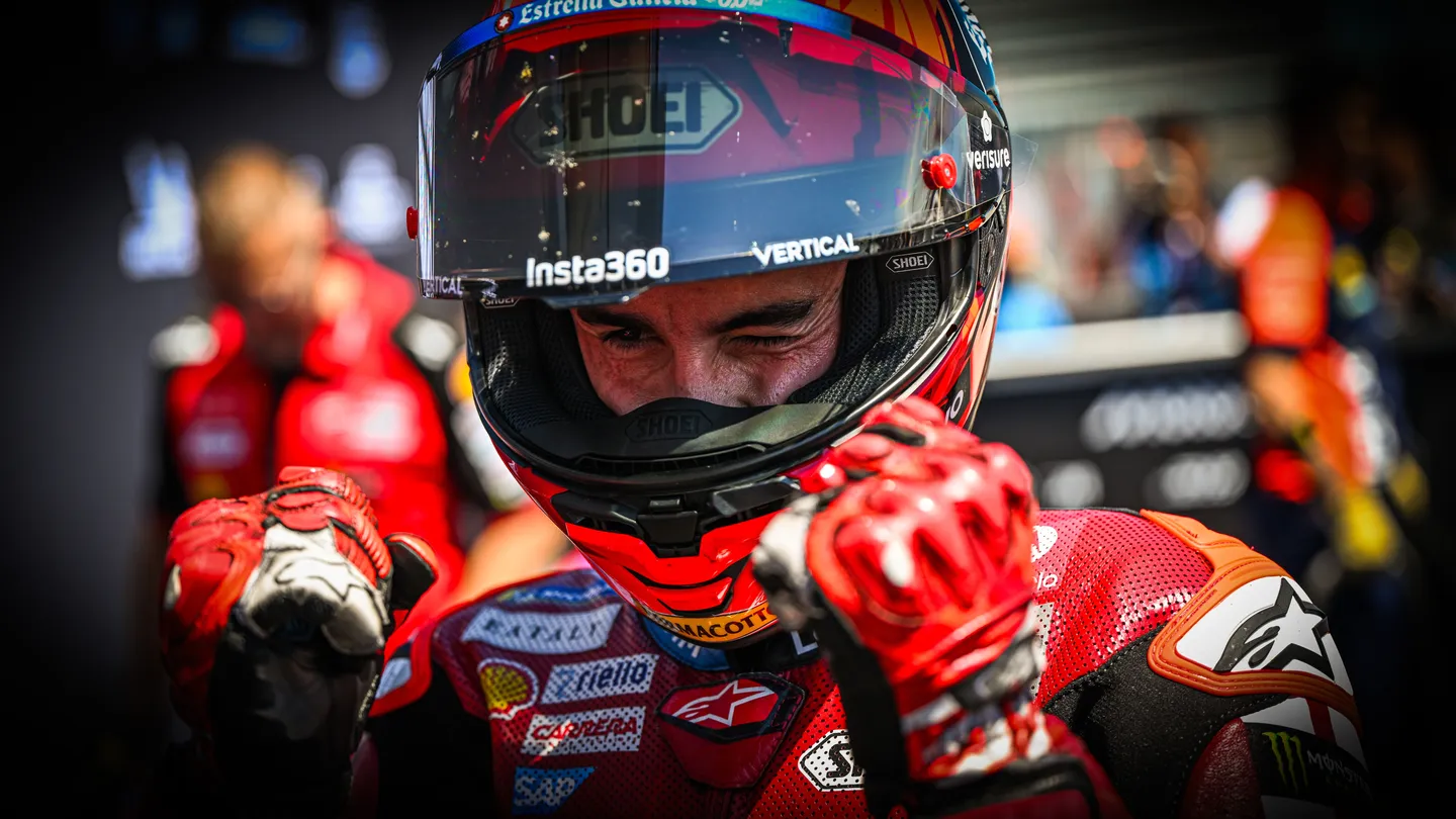 Marc Marquez mengenakan helm dan baju balap Ducati sambil mengepalkan kedua tangan.