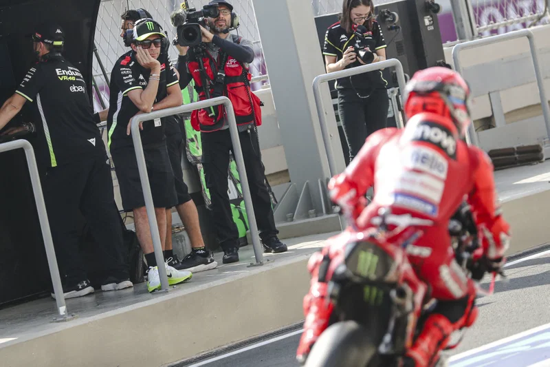 Valentino Rossi mengamati dari depan garasi VR46 saat Marc Marquez melintas dengan motor Ducati di pit lane.
