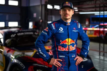 Max Verstappen mengenakan baju balap biru dengan logo Red Bull di depan mobil balap GT.