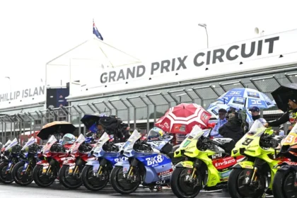Deretan motor MotoGP dan kru dengan payung di lintasan basah Phillip Island.