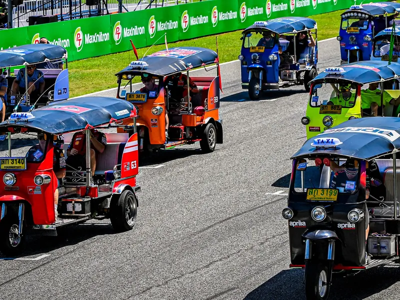 Deretan tuk-tuk dengan livery tim MotoGP mengikuti parade di lintasan sirkuit.