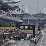 Mobil F1 dan kru tim berkumpul di pit lane Sirkuit Sepang di bawah langit mendung