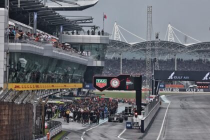 Mobil F1 dan kru tim berkumpul di pit lane Sirkuit Sepang di bawah langit mendung